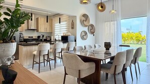 A modern kitchen with a central island, dining area with chairs, and large windows. - 3BR Punta Cana Villa Near Beach & Mall| Yellowkey (punta cana)
