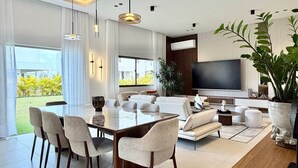 A modern living room with a dining area, a large TV, and a view of a garden. - 3BR Punta Cana Villa Near Beach & Mall| Yellowkey (punta cana)