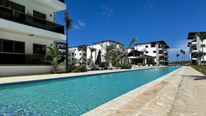 A swimming pool with clear blue water, surrounded by modern buildings with balconies and outdoor seating areas. - 3BR Punta Cana Villa Near Beach & Mall| Yellowkey (punta cana)