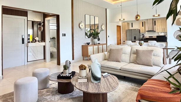 A modern living room with a sofa, coffee table, and ottomans. There is a kitchen in the background with a refrigerator and cabinets. - 3BR Punta Cana Villa Near Beach & Mall| Yellowkey (punta cana)