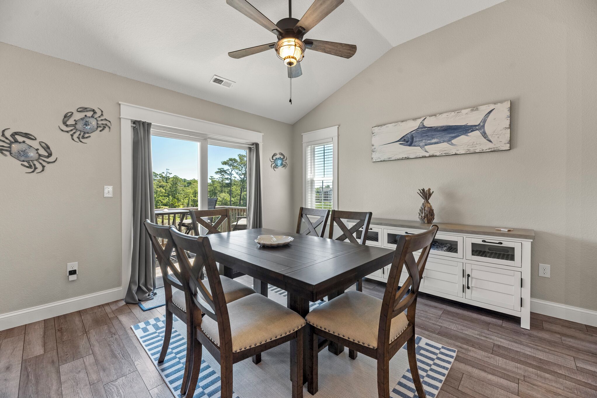 A dining area with a table, chairs, a ceiling fan, and a kitchen area with cabinets.