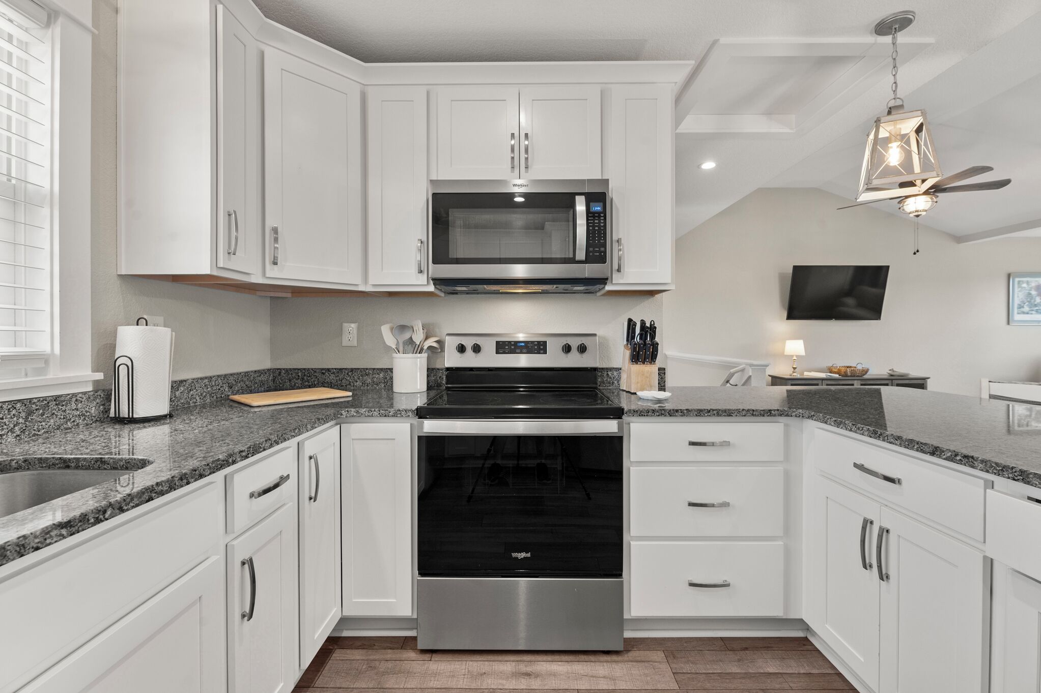 A modern kitchen with white cabinets, a stainless steel microwave, a built-in oven, granite countertops, and a ceiling fan.