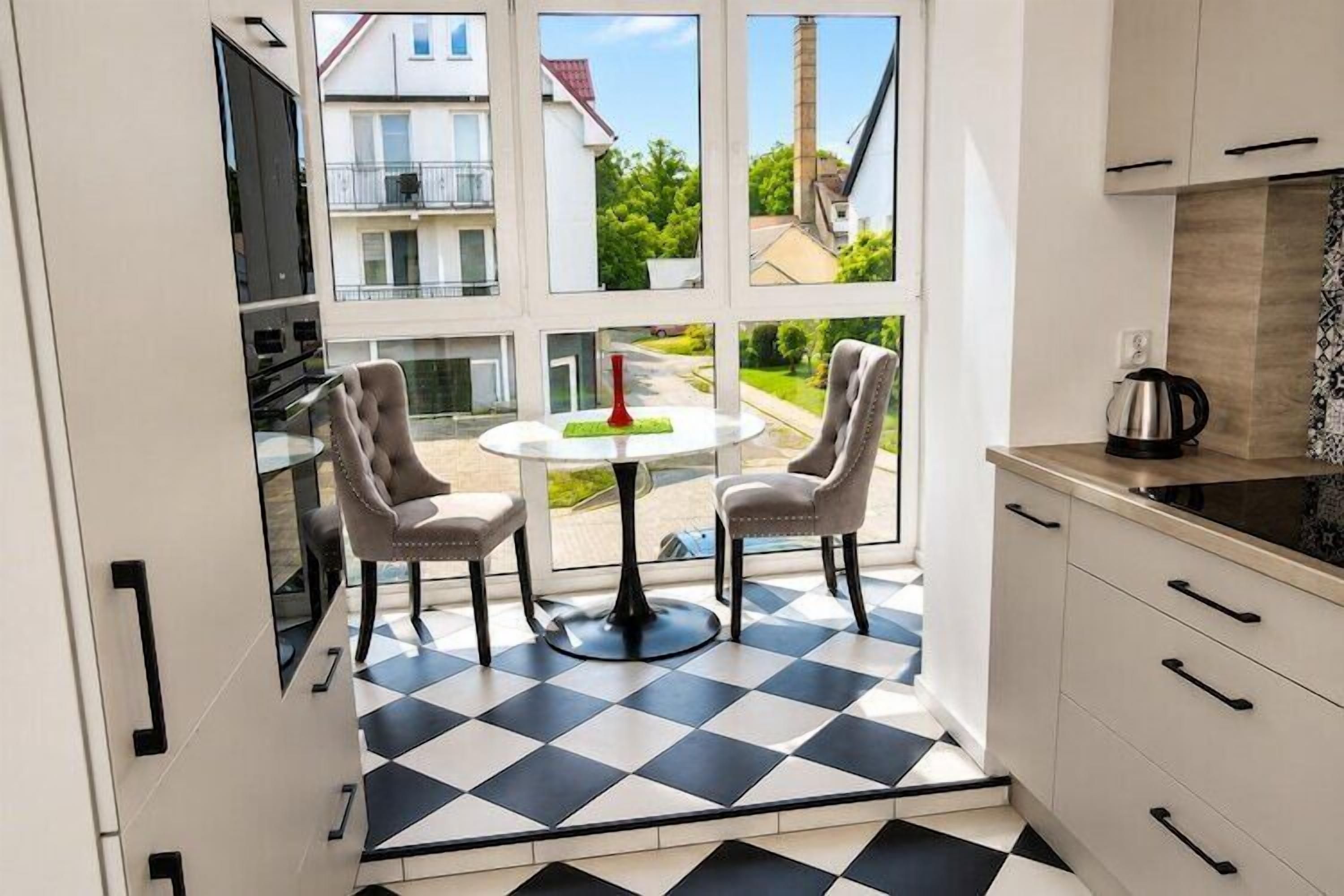 Une cuisine avec un carrelage à motifs, deux chaises, une table et une vue sur un quartier résidentiel grâce à de grandes fenêtres.