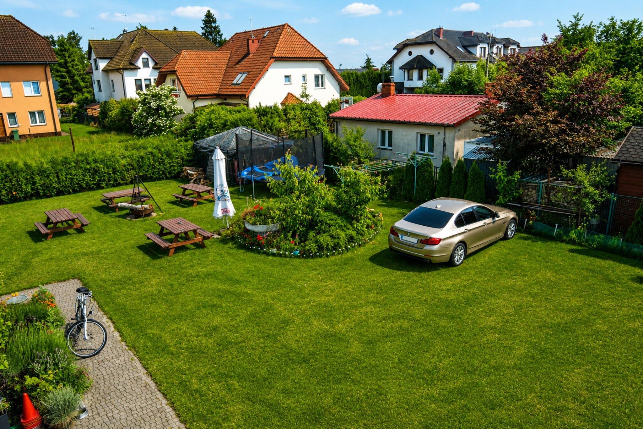 A residential area with houses, a car, and a garden with picnic tables and a swing set.