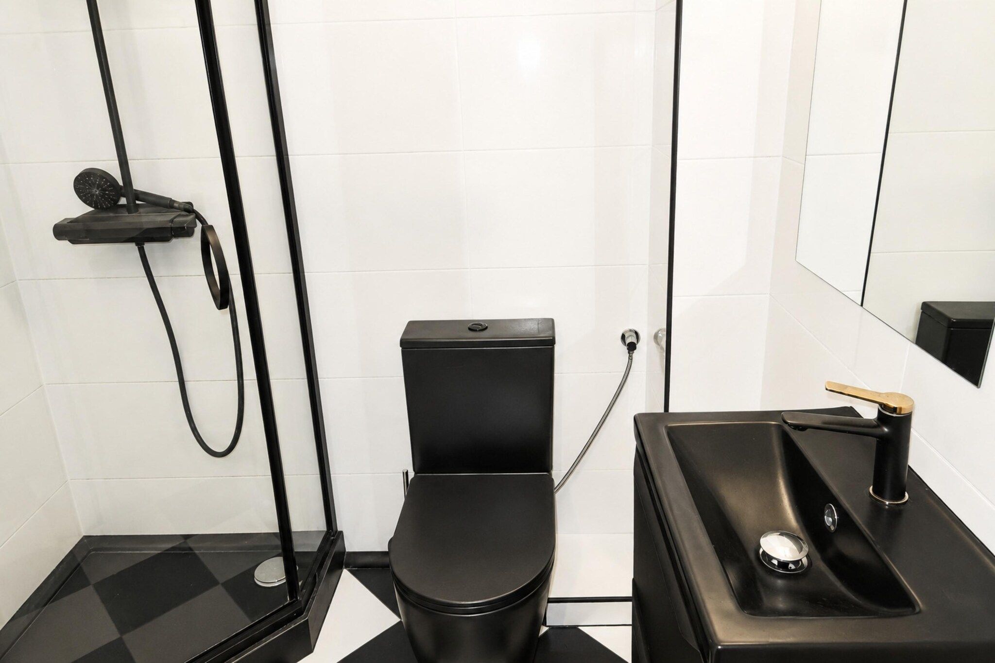 Een moderne badkamer met een zwart toilet, een douchecabine en een wastafel met een gouden kraan.