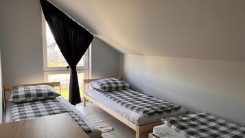 Une chambre de dortoir avec deux lits simples, un bureau en bois et une fenêtre avec des rideaux.