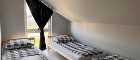 A dormitory room with two single beds, a wooden desk, and a window with curtains.