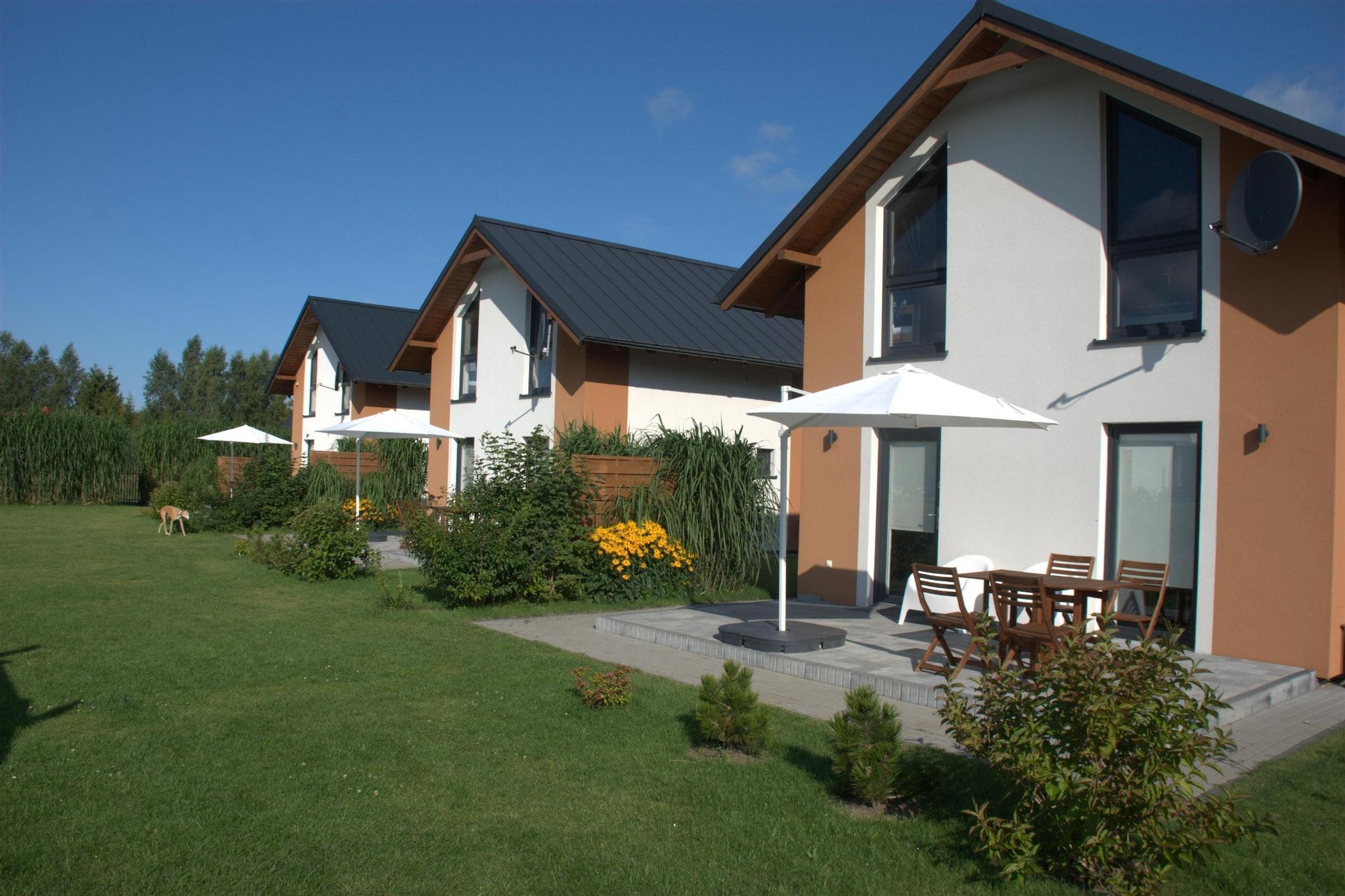 A modern residential building with a patio area, outdoor seating, and a well-maintained lawn.