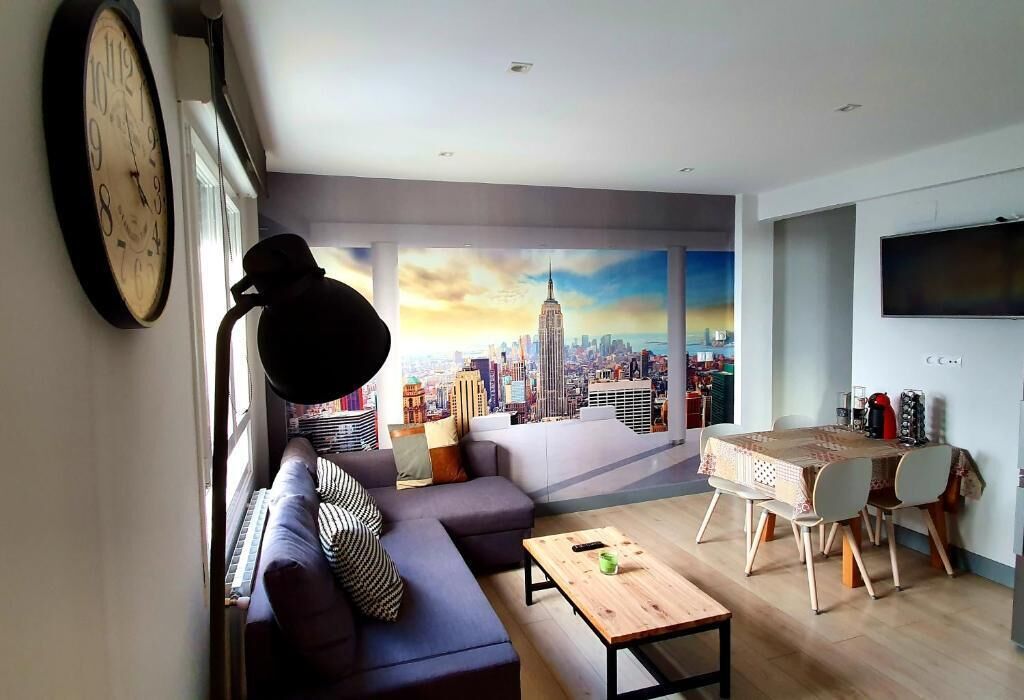 Een moderne woonkamer met een bank, een salontafel, een eettafel met stoelen, een grote klok en een muurschildering van een stadsgezicht.