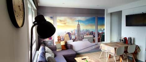 A modern living room with a sofa, a coffee table, a dining table with chairs, a large clock, and a cityscape mural on the wall.