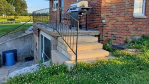 Une maison en briques dotée d’un espace extérieur couvert, d’un escalier menant à un garage et d’un petit jardin.