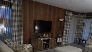 Un salon comprenant un canapé, un pouf et un téléviseur posé sur un meuble en bois.