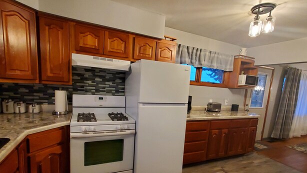 Une cuisine avec des meubles de rangement en bois, une cuisinière à gaz, un réfrigérateur et un four à micro-ondes.
