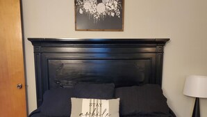 Une chambre à coucher avec une tête de lit en bois foncé, un lit avec une literie noire, deux oreillers, un tableau encadré au-dessus du lit et une lampe de chevet.