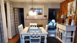 Un coin repas avec une table et des chaises, un tapis noir, un plancher en bois, un meuble blanc et un miroir au-dessus de la table.