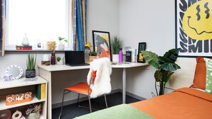 Un dormitorio moderno con escritorio, silla, cama y ventanas amplias.