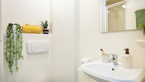 Un baño con lavamanos blanco, un espejo, toallero con una toalla amarilla, dispensador de jabón y un porta cepillos de dientes.