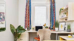 Una habitación con escritorio, silla, cama y varias plantas.