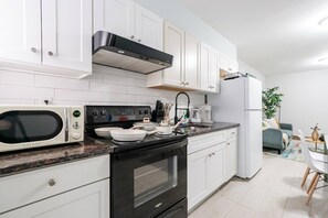 A modern kitchen with white cabinets, a black stove, a microwave, and a refrigerator.