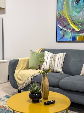 A living room with a grey sofa, a yellow coffee table, a vase with flowers, and a remote control.