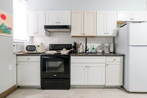 Une cuisine avec des meubles blancs, une cuisinière noire, un four à micro-ondes et un réfrigérateur.