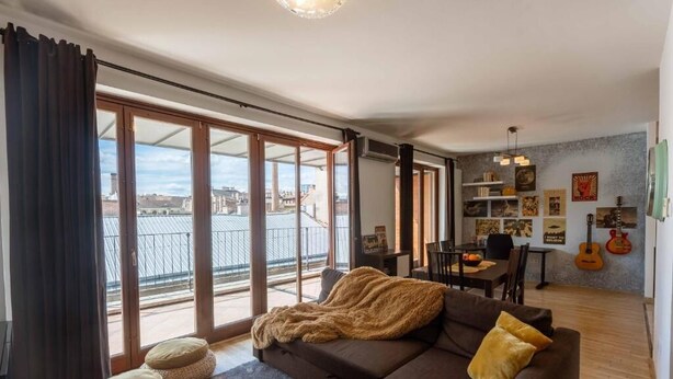 Een moderne woonkamer met een bank, poefs, een eethoek en een balkon met uitzicht.