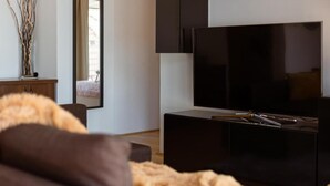 Een moderne woonkamer met een grote flatscreen televisie, donkere meubels en een decoratieve vaas op een houten kast.