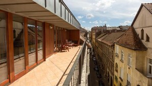 Een gebouw met een balkon, houten meubels en uitzicht op omliggende historische panden.