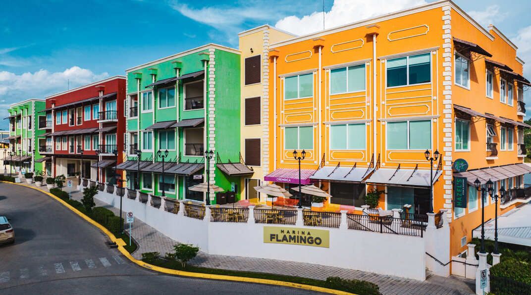 A row of colorful buildings with balconies, a street, and a sign for 'Marina Flamingo.'