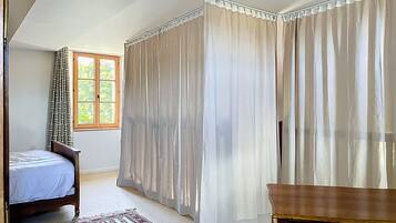 A bedroom with a bed, a window, curtains, a wooden nightstand, and a patterned rug.