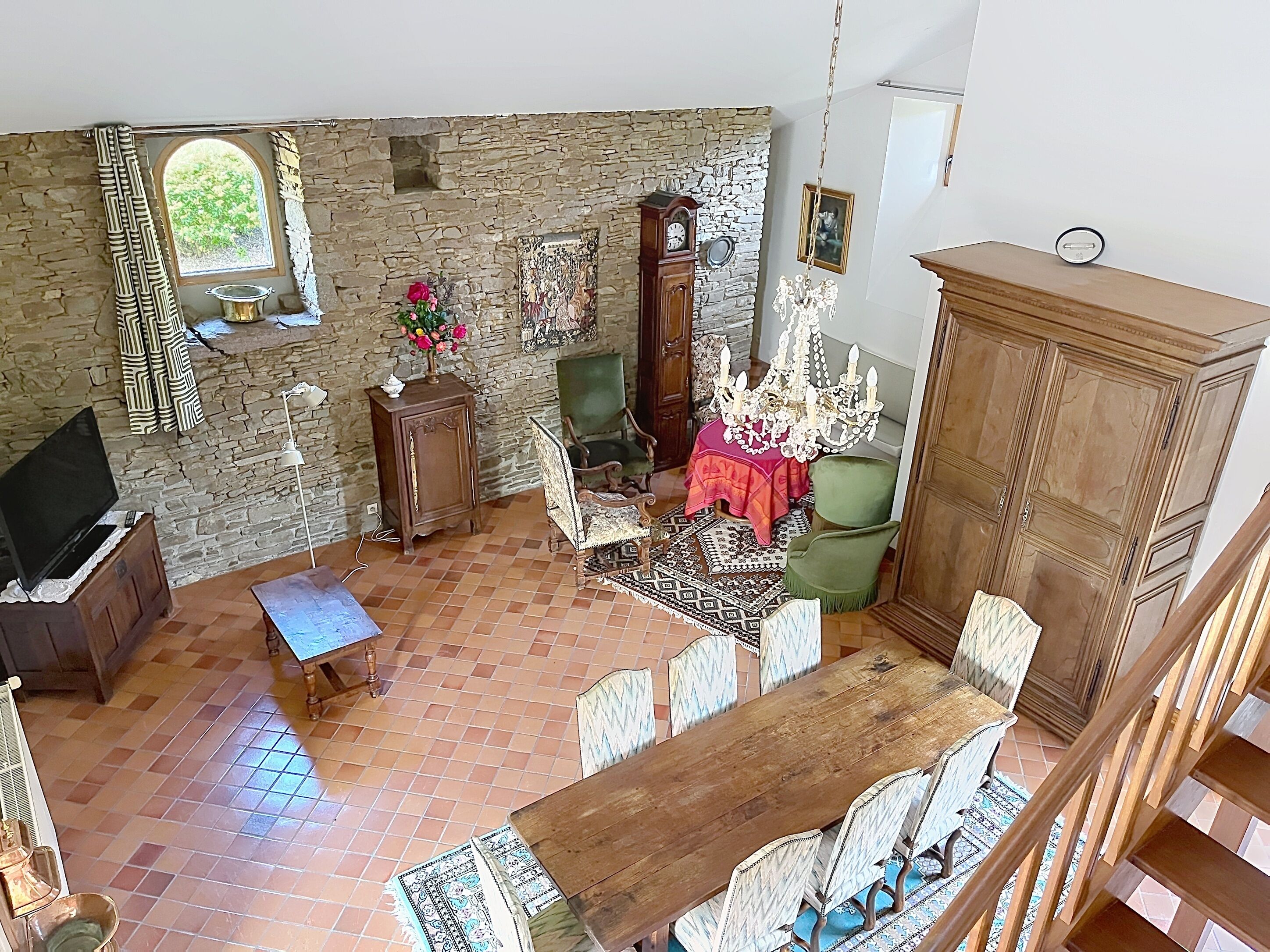 A rustic room with a stone wall, a wooden table with chairs, a television, a chandelier, and a wooden cabinet.