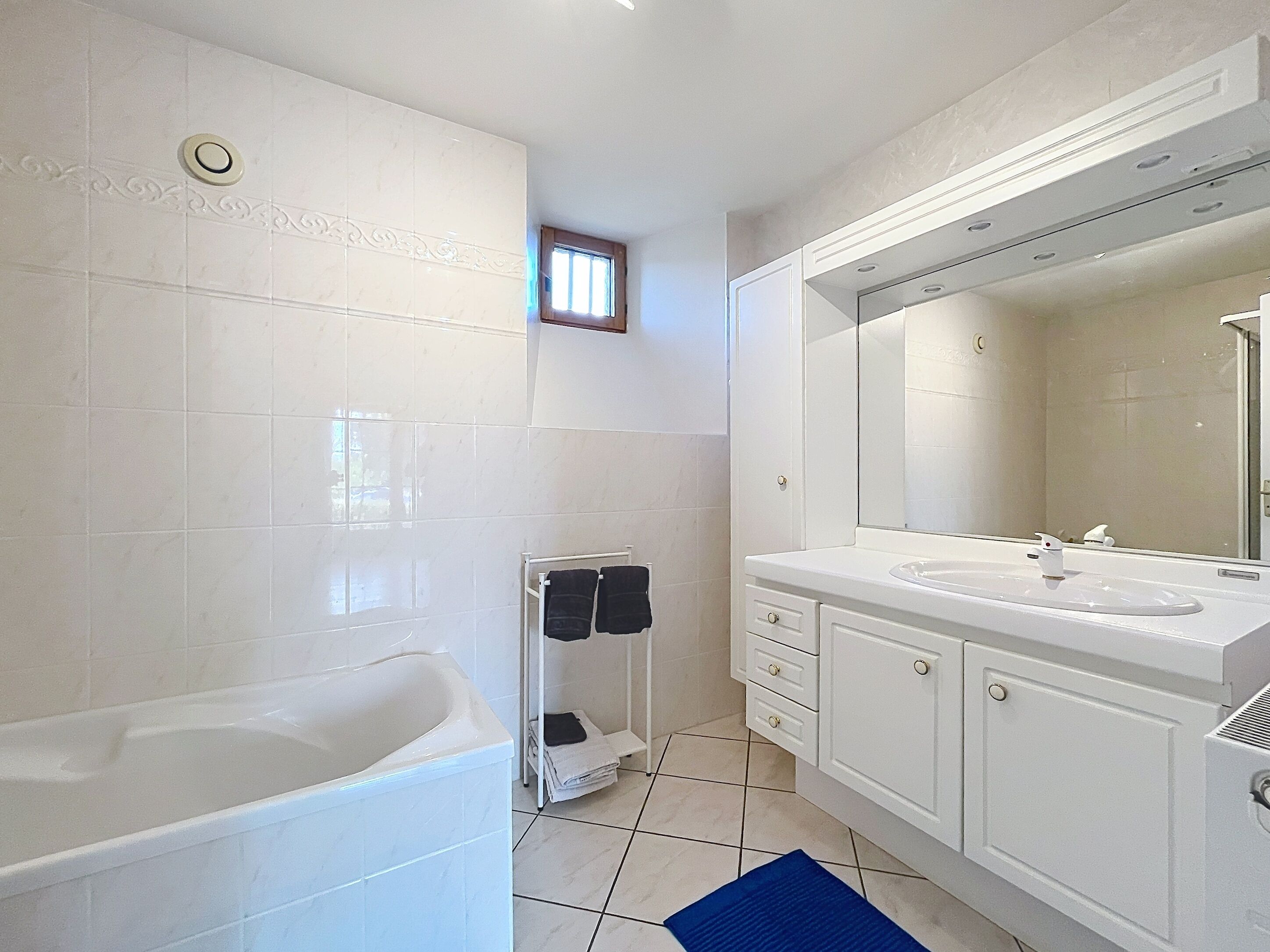 A bathroom with a bathtub, a sink, a mirror, and a towel rack.