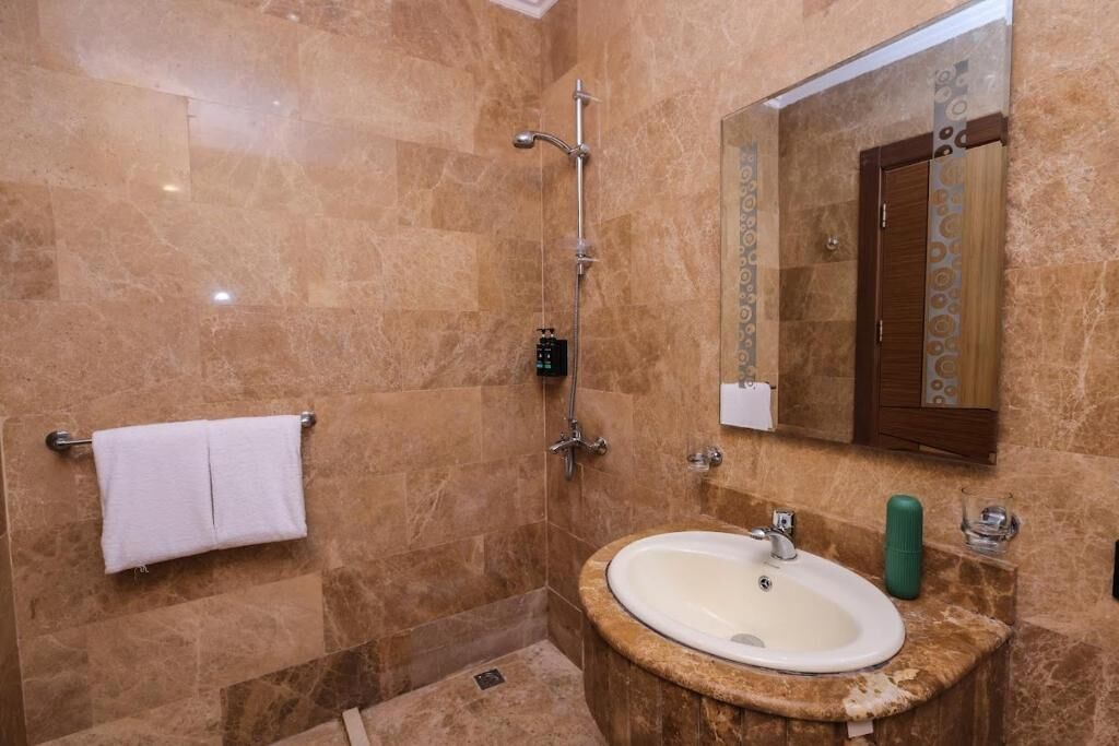 A bathroom with a marble wall, a sink, a mirror, and a towel rack.