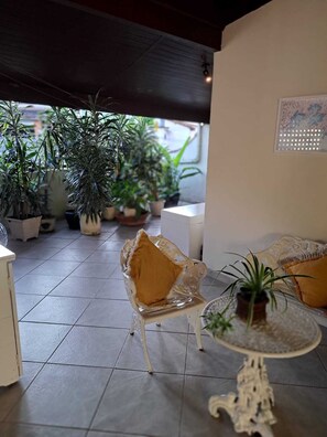 A covered patio area with potted plants, a white chair with a yellow cushion, and a small table with a plant. - Family home in a gated community. FAMILY ENVIRONMENT. (Angra dos Reis)