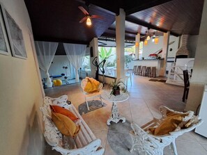 A covered outdoor seating area with white furniture, a small table, and a ceiling fan. - Family home in a gated community. (Angra dos Reis)