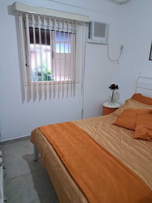 A bedroom with a bed, a window with blinds, a bedside table with a vase, and a wall-mounted air conditioner. - Family home in a gated community. (Angra dos Reis)