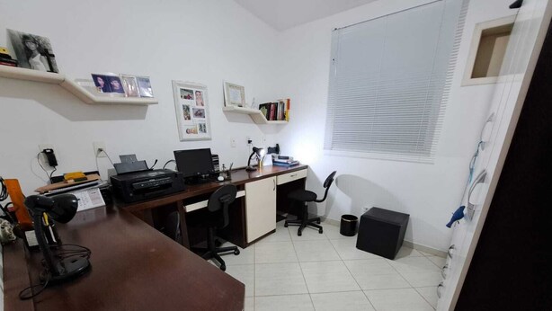 Ein kleines Büro mit Schreibtisch, Computer, Stuhl und Regalen mit Fotos.
