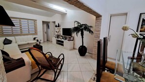 Ein Wohnzimmer mit einer Couch, einem Schaukelstuhl, einer TV-Konsole, einem Topfpflanzen und einem Glastisch mit Stühlen.