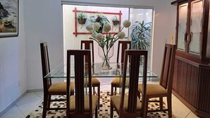 Ein Essbereich mit einem Glastisch, Holzsesseln, einer Vase mit Blumen und Blick durch eine Glastür.