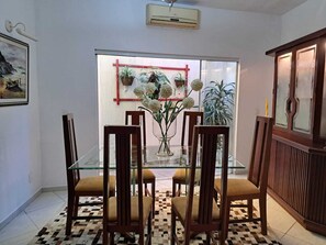 A dining area with a glass table, wooden chairs, a vase with flowers, and a view through a glass door. - Family home in a gated community. (Angra dos Reis)