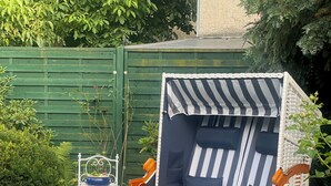 En trädgård med en trästol med randiga kuddar, en vit lykta och krukväxter.