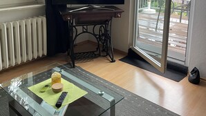 Ett vardagsrum med en tv, ett soffbord i glas, ett element och en skjutdörr i glas som leder ut till ett utomhusområde.