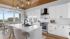 Een moderne keuken met witte kastjes, een groot eiland, roestvrijstalen apparatuur en een houten plafond.