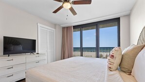 A bedroom with a bed, a television, a ceiling fan, a window with a view, and a balcony. - 🌊 Lei Lani 104 | Gulf Front Orange Beach | 2 Pools + Ole River Access (Orange Beach)