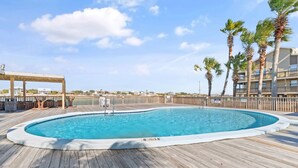 A swimming pool with a wooden deck, surrounded by palm trees and a building with balconies. - 🌊 Lei Lani 104 | Gulf Front Orange Beach | 2 Pools + Ole River Access (Orange Beach)
