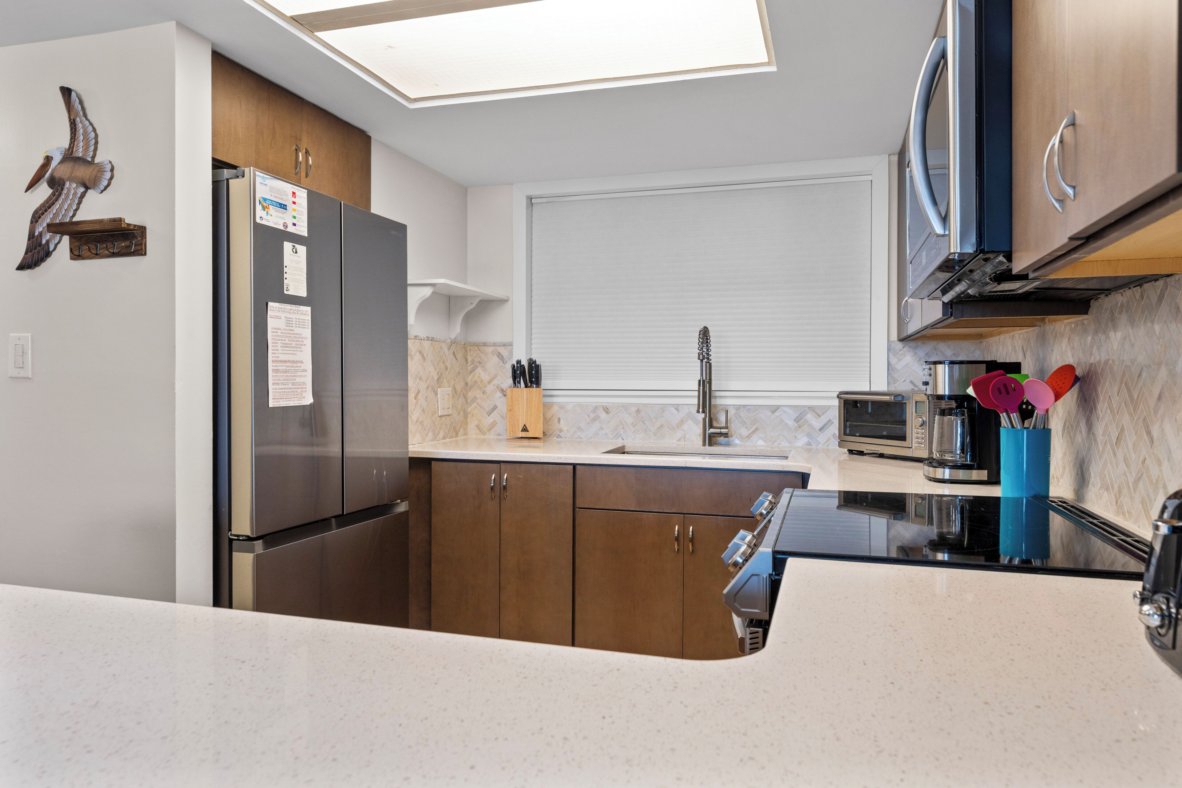 Una cocina moderna con refrigerador de acero inoxidable, armarios de madera, microondas y un lavamanos.