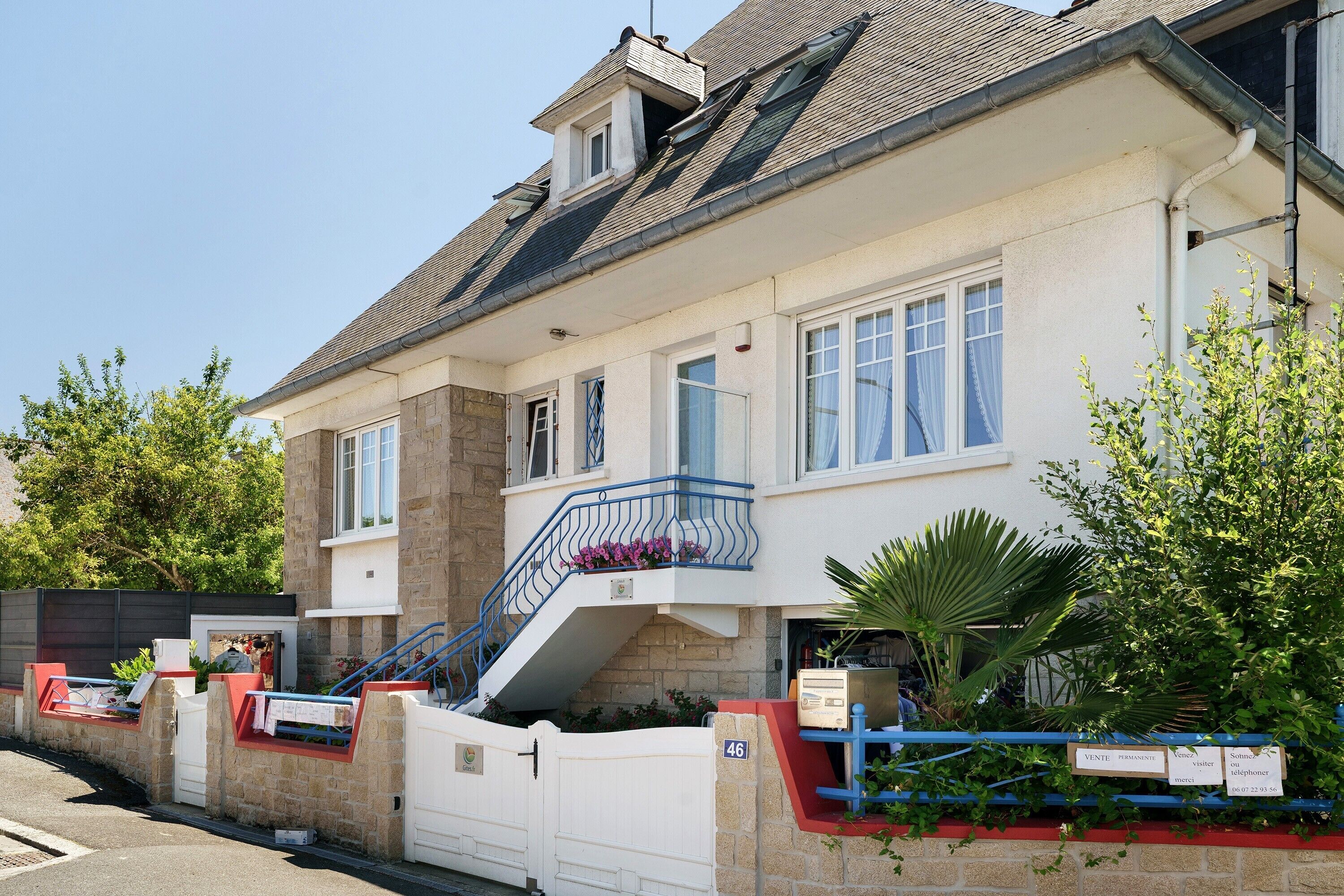 Un edificio a due piani con facciata in pietra, un balcone con ringhiere blu e una scala che conduce al piano superiore.