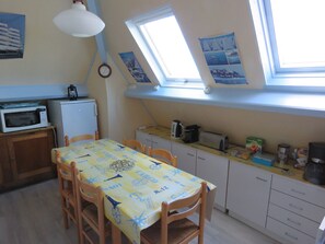 Eine kompakte Küche mit Esstisch, Stühlen, einer Mikrowelle, einem Kühlschrank und einem Fenster mit Dachfenstern.