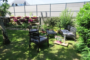 Ein gepflegter Garten mit verschiedenen Kübelpflanzen, einer Holzbank und einem Tisch.