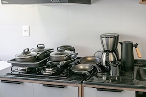 Eine Küche mit Herd, Töpfen, Pfannen, einer Kaffeemaschine und einem Wasserkocher.